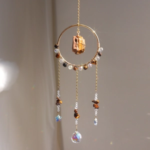 Detail of sun catcher featuring golden wire, brown stones, and multifaceted crystal prism