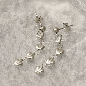 Détail de boucles d'oreilles cœurs argentés avec texture polie et design en cascade