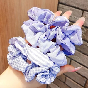 Set of purple floral and striped fabric scrunchies held in hand against a brick wall