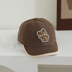 Detailed macro view of the embroidered bear patch on a dark brown cotton baseball cap