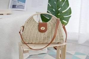 Detail of hand-woven half-moon straw bag with brown leather flap and golden metal lock