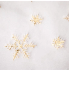 Close-up of white plush Christmas tree skirt featuring golden sequin snowflake patterns