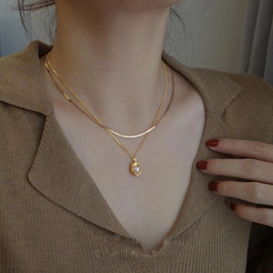 Zweilagige goldene Schlangenkette mit unregelmäßigem Perlenanhänger an einem Model