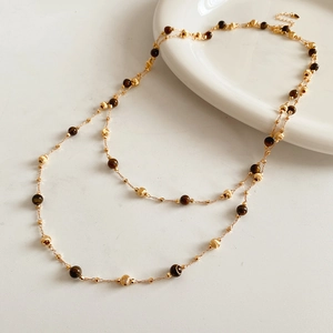 Detail of layered gold-plated necklace featuring brown tiger eye beads on white plate