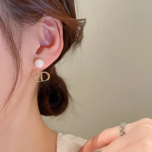 Elegant gold letter D stud earrings with white pearls for women in soft indoor lighting