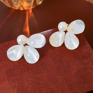 Detailed close-up of pearl flower earrings with shell petals on textured brown leather