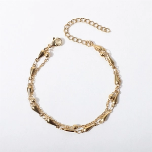 Detail of gold double-layer bracelet with metal beads and teardrop charm on white background