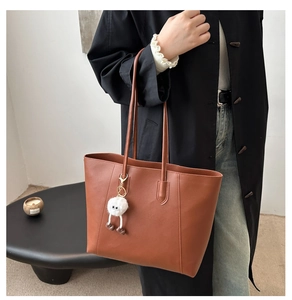 Sac fourre-tout en cuir marron avec breloque en peluche blanche dans un décor minimaliste