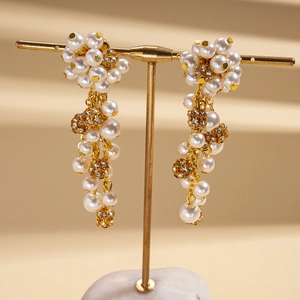 Detail of long gold earrings with faux pearls and rhinestone-studded spheres on a stand