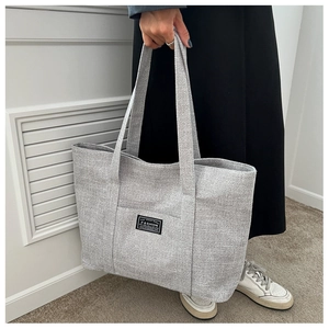 Detail view of large light grey canvas tote bag with fashion tag held by a person