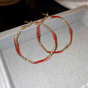 Macro detail of red enamel gold-plated hoop earrings on a grey velvet display tray