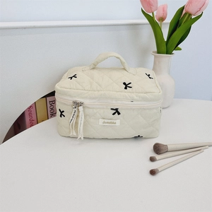 Detailed macro view of cream quilted makeup bag with black bow embroidery and sturdy handle