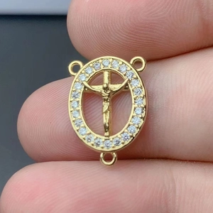 Golden St. Benedict Guadalupe cross pendant with zircon stones held by hand close-up