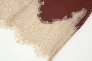 Detail of burgundy satin fabric with off-white eyelash lace trim and fine texture