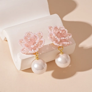 Pink crystal flower earrings with white pearls on a minimalist white stone display