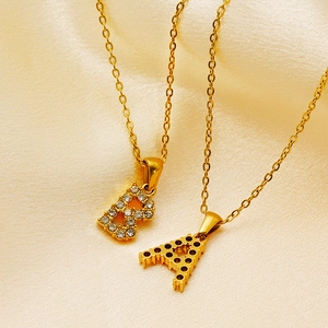 Macro shot of gold-plated A and B letter pendants with cubic zirconia on beige silk