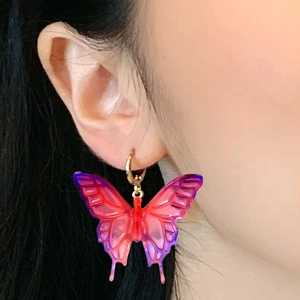 Détail d'une boucle d'oreille papillon en résine violette avec anneau doré sur l'oreille