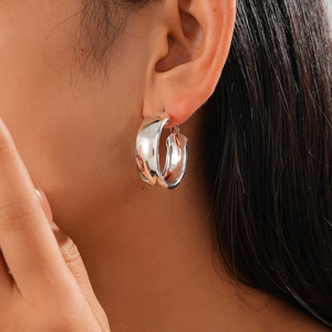 Close-up of a wide silver-colored metallic hoop earring worn by a model in detail