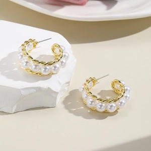 Detailed shot of gold twisted hoop earrings with white pearls on a stone base