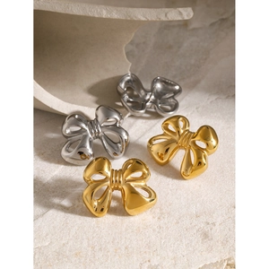 Elegant 18k gold and silver bow stud earrings on a textured stone display