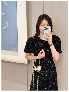 Close-up of golden lip-shaped mini metal crossbody bag with chain on a sequin dress