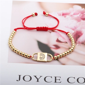 Detailed close-up of a red cord bracelet with gold beads and a zircon lock charm