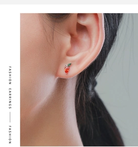 Close-up of small orange carrot earrings with green leaves worn on a model's ear
