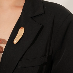 Macro detail of irregular golden liquid metal brooch on a black suit lapel