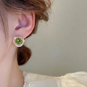 Detail view of a vintage gold earring with green zircon on a model's ear