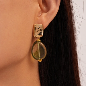 Detail view of green acrylic drop earrings with gold textured square studs on a model
