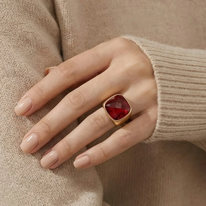 Detail view of a vintage gold ring with a large square-cut red crystal on a soft beige knit