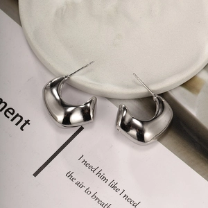Detailed close-up of thick silver C-shaped hoop earrings on a minimalist white display