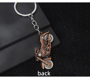 Rear view of vintage bronze motorcycle keychain with silver wheels on a dark surface