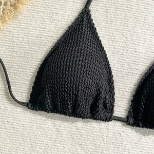 Close-up of black seersucker triangle bikini top with pleated texture on beige beach mat