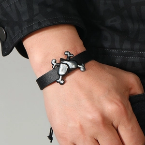 Close-up of punk style black braided leather bracelet with vintage silver cross charm