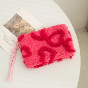 Close-up of plush pink vanity bag with red 3D hearts and a woven wrist strap