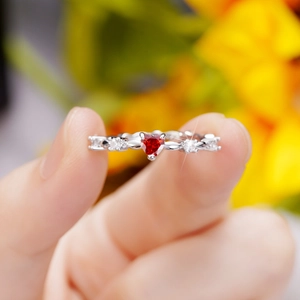 Close-up of elegant red heart-shaped zircon ring with white stones held by fingertips