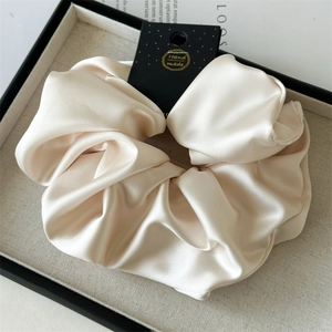 Detailed macro view of champagne satin scrunchie with a gold-stamped handmade tag