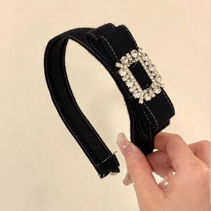 Détail d'un serre-tête en velours noir avec boucle en strass tenu à la main