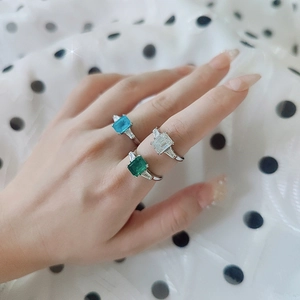 Three colors of emerald cut moissanite rings shown on a hand with polka dot background