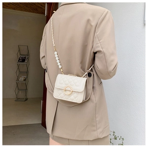 Detailed view of mini cream quilted crossbody bag with pearl chain on model