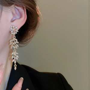 Détail de boucles d'oreilles pendantes dorées avec motifs feuilles et cristaux brillants