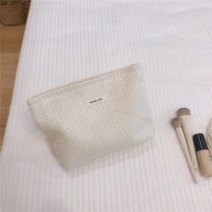 Close-up of cream tweed woven cosmetic bag with simple wish label and soft texture