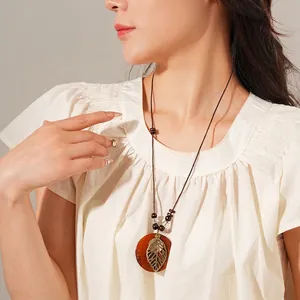 Collier bohème avec feuille évidée et perles en bois porté sur fond minimaliste