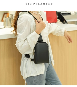 Detail of minimalist black crossbody chest bag with wide strap on a model with wood background