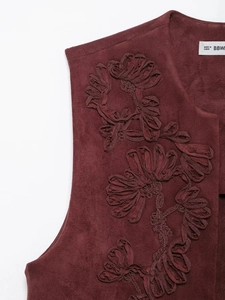 Dettaglio del ricamo floreale su gilet in camoscio bordeaux con cuciture raffinate