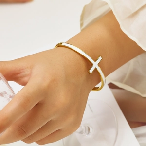 Bracciale rigido aperto in acciaio dorato con croce in smalto bianco su modella
