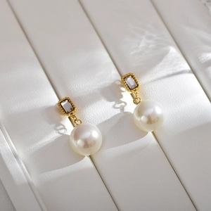 Detail of vintage gold pearl earrings with rectangle crystal on a white leather tray