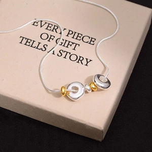 Minimalist snake chain necklace with gold and silver ring pendants on a gift box
