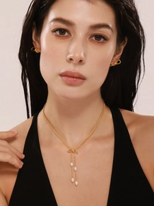 Détail d'un mannequin portant une parure de boucles et collier doré à nœud et perles